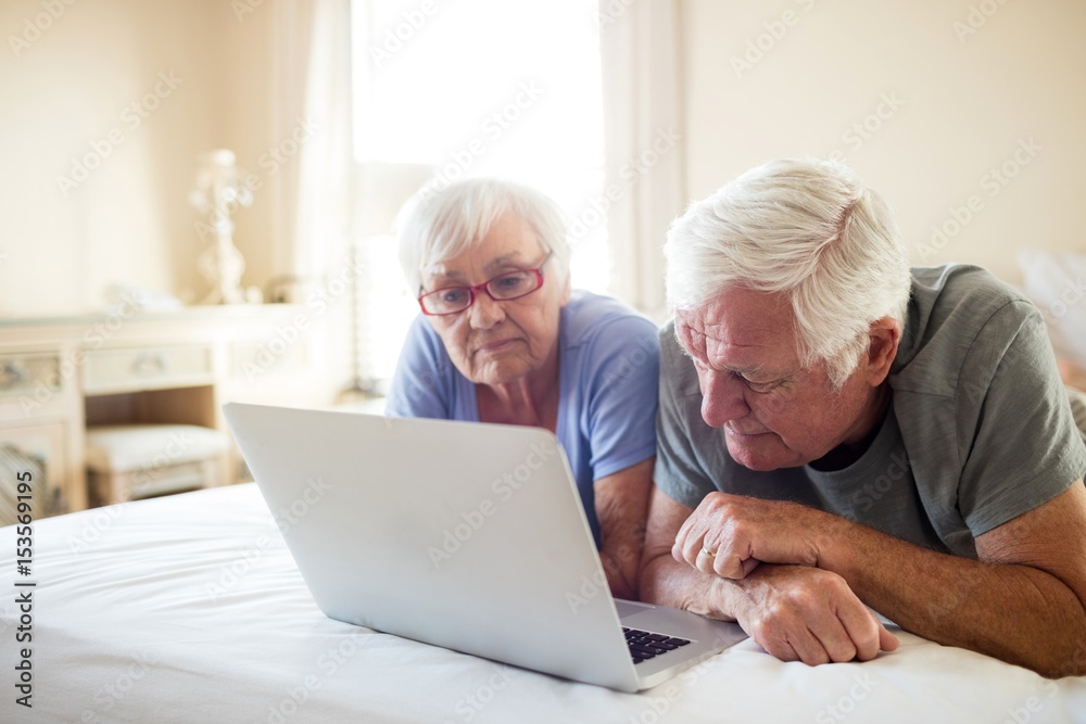 Senior couple using laptop on bed in bedroom Senior couple using laptop on bed in bedroom