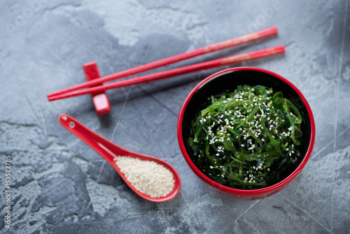 Red tableware with seaweed salad and sesame seeds on a grey stone background, high angle view, horizontal shot