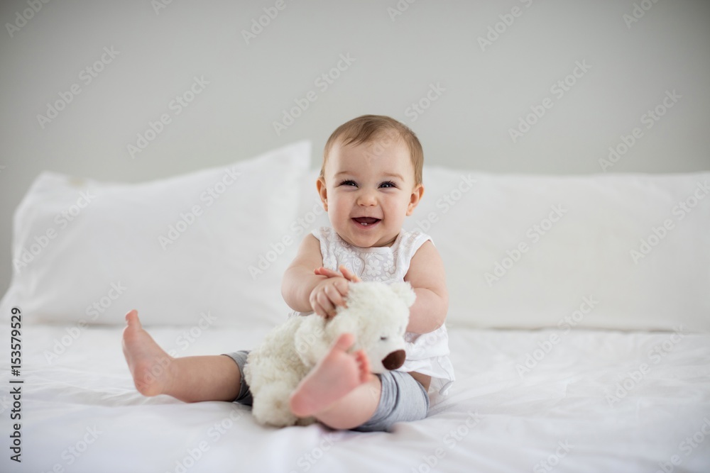 Cute baby girl playing with soft toy on bed - obrazy, fototapety, plakaty 