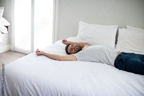 Man lying on bed with arms up on bed