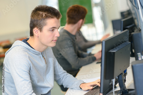 male teenage student working at computer at school