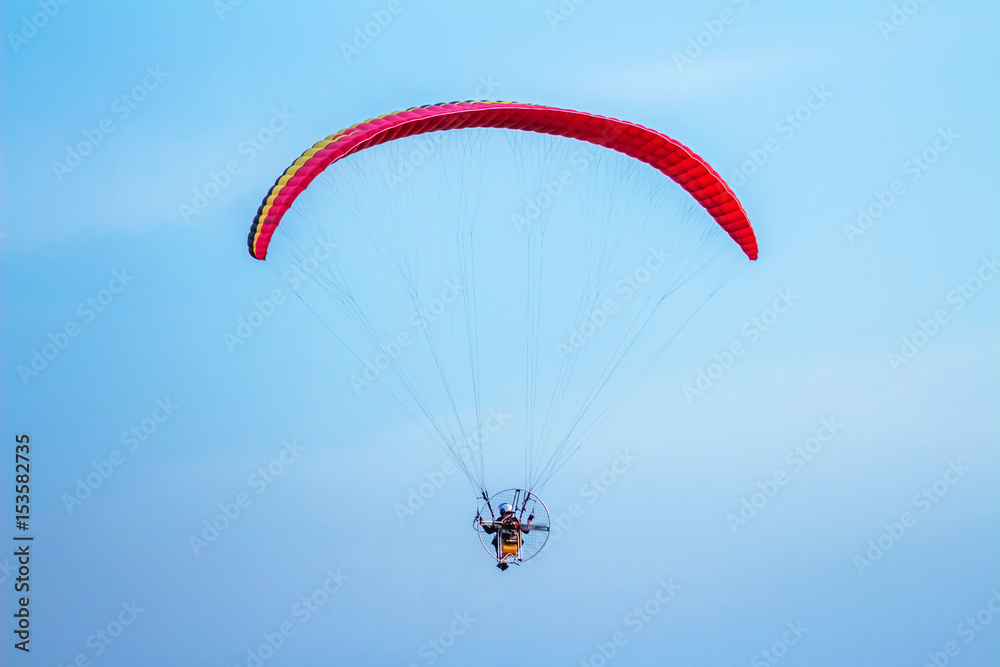 Rear view of man flying with paramotor glider parachute on beautiful blue sky Rear view of man flying with paramotor glider parachute on beautiful blue sky