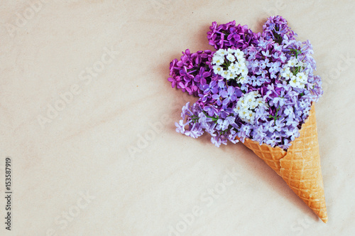 Ice cream waffle cone with lilac flowers on the craft paper background