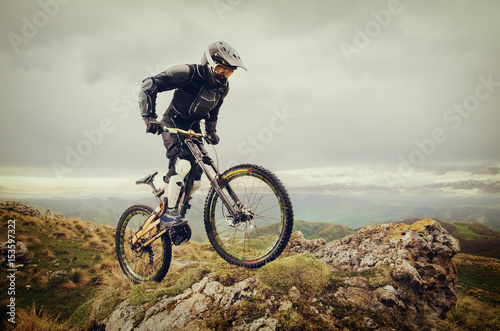 Fotografie Ryder in full protective equipment on the mtb bike climbs on a rock against the