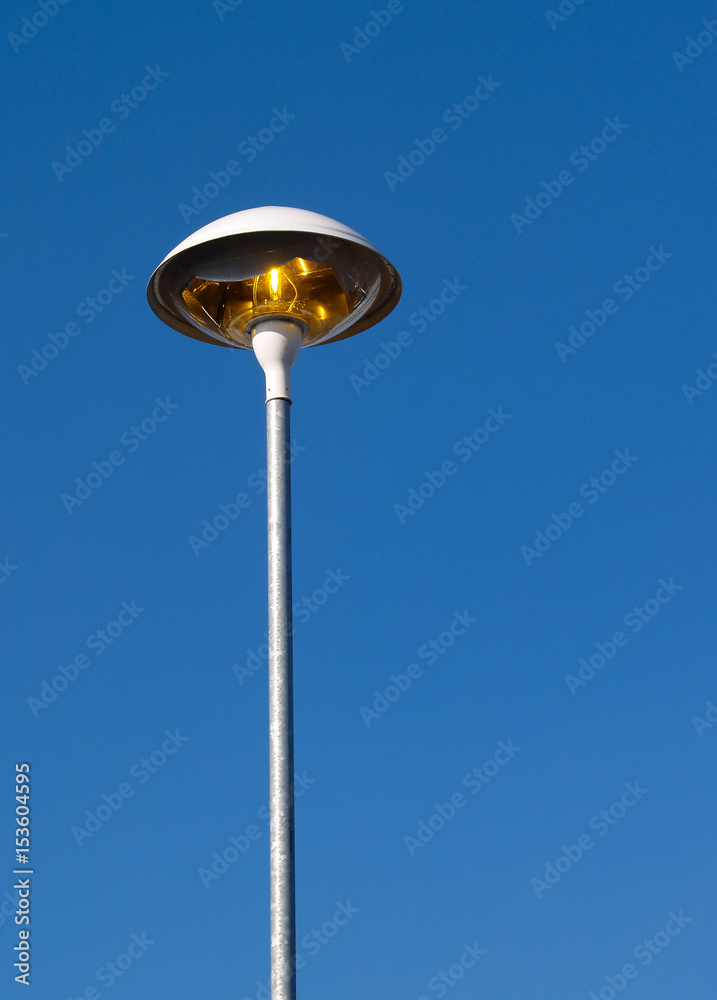 Tall light (in a supermarket car park) switched on even though it is bright daylight. Tall light (in a supermarket car park) switched on even though it is bright daylight.