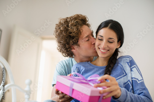 Woman receiving gift  in pink box from boyfriend in their bedroom
