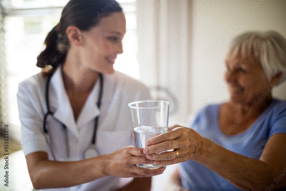 Doctor serving a water glass to senior woman 