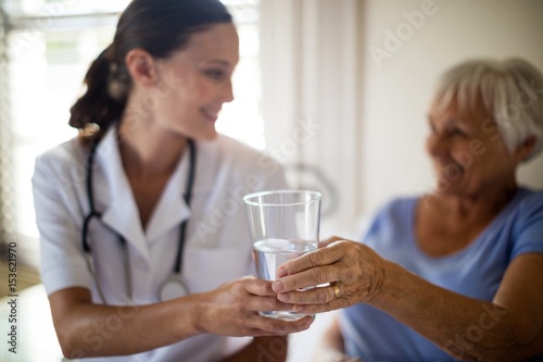 Doctor serving a water glass to senior woman 