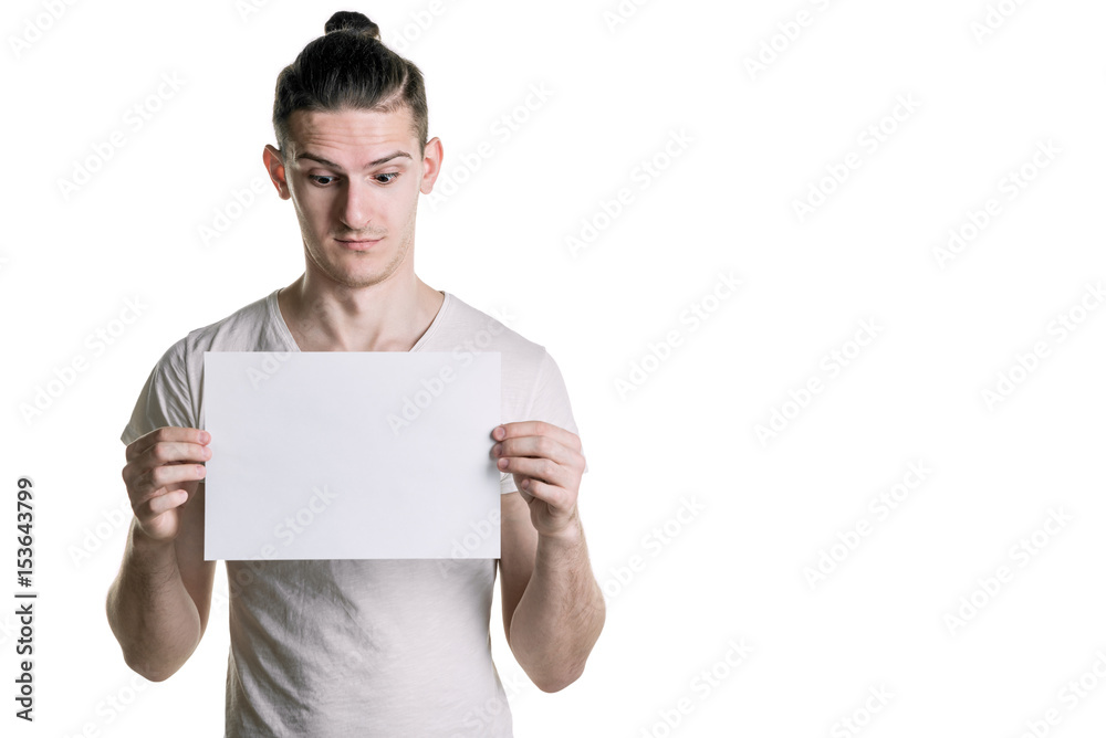 A young handsome guy with a blank sheet of paper, looking at the paper with astonishment. Place for signature, text. Horizontal frame A young handsome guy with a blank sheet of paper, looking at the paper with astonishment. Place for signature, text. Horizontal frame