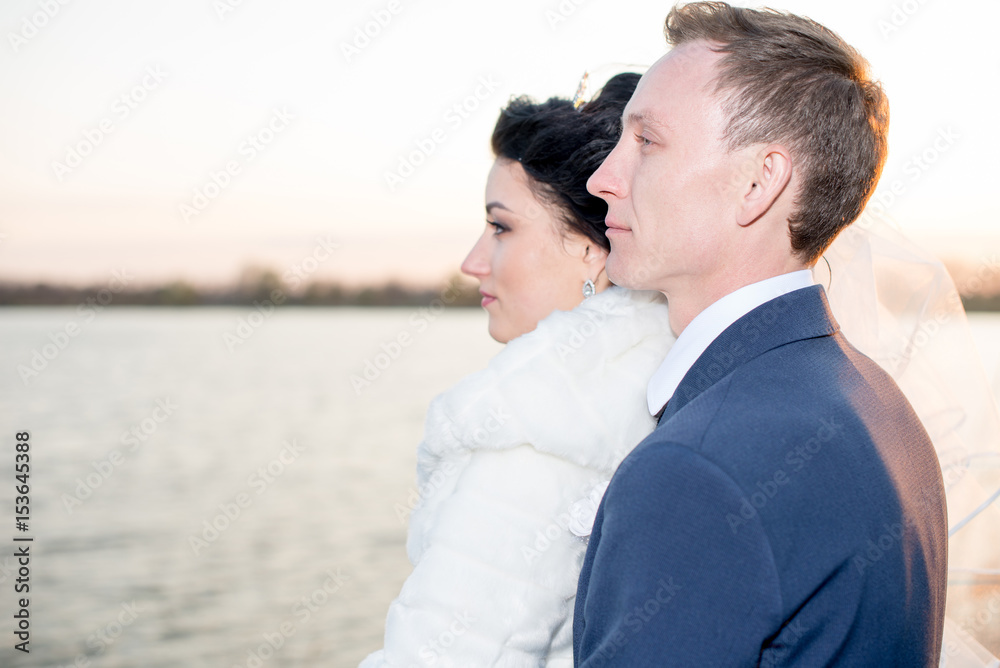 romantic landscape, the newlywed couple posing at sunset near the river, the bridegroom holds the hand of a bride