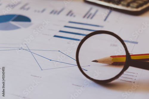 Many charts and graphs with pencil, magnifying glass, calculator, clock. Reflection light and flare. Concept image of data gathering and statistical working.