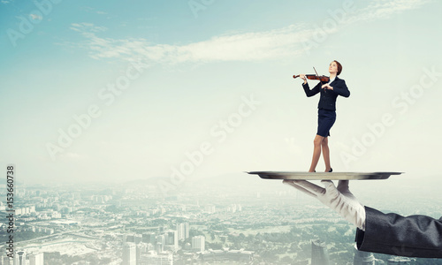 Attractive businesswoman on metal tray playing violin aginst cityscape background