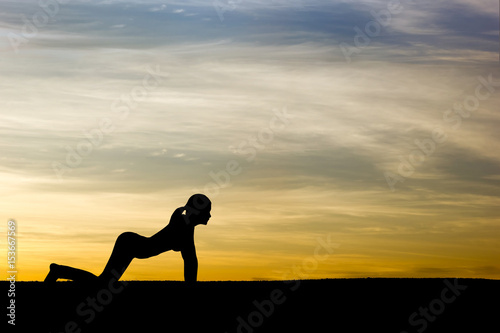 Woman practicing Cow yoga pose outdoors over sunset sky background.