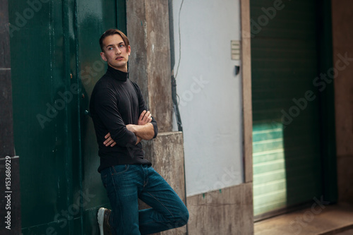 Young man relaxed stands near the wall of the house.