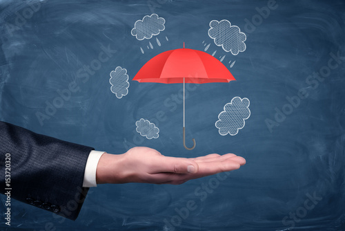 A businessman s hand turned up and a small red umbrella hovering above it on chalkboard background.