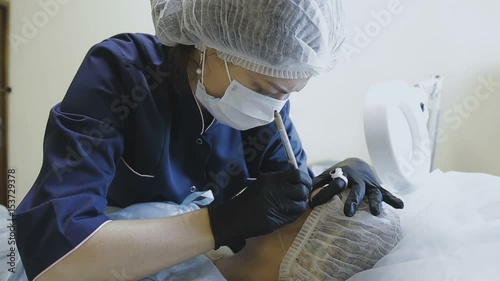 A female employee of a cosmetology clinic makes a microblasting routine to a female patient photo