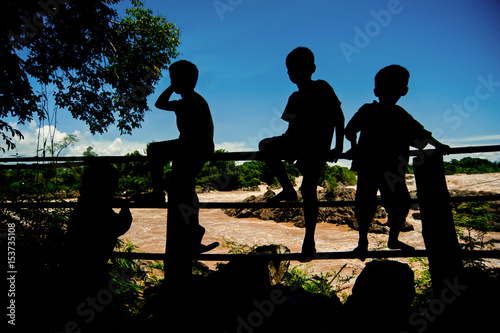 Silhouette Little boy sitting on a fence at Khone Phapheng water fall or mekong river in champasak southern of laos one of the biggest and beautiful waterfall in asia and world photo