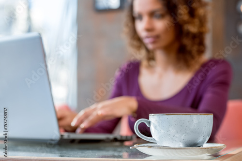 Mood for the day. Selective focus on a cup on the table woman using her laptop on the background