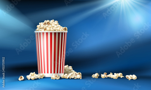 Vector illustration of a red and white cardboard bucket with popcorn in a realistic style isolated on a blue background with light rays