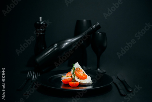 tomato and mozzarella with spice, sauce and wine on black background
