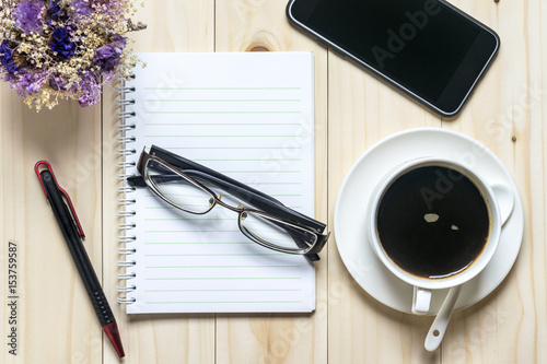 Flat lay desk with coffee, notebook, smartphone, eyeglasses and flowers