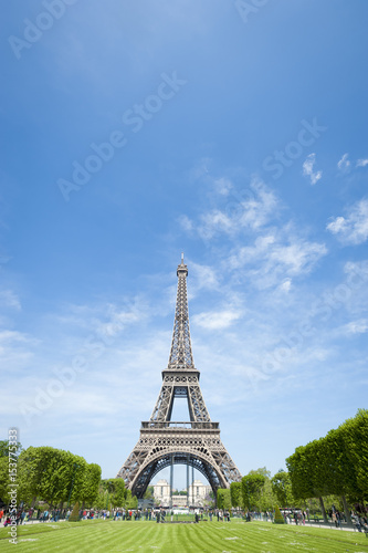 Bright daytime scenic view of the Eiffel Tower in Paris, France, with spring greenery on the Champs de Mars under clear blue sky © lazyllama