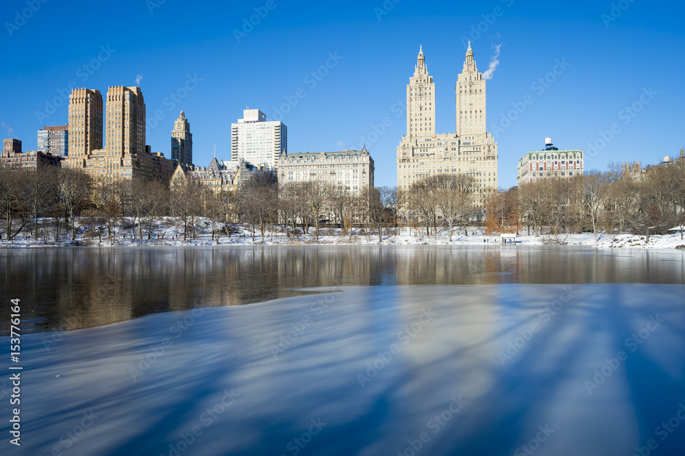 Scenic view of the Upper West Side skyline reflecting in the ice of the frozen Central Park lake the morning after a winter snow storm in New York City
