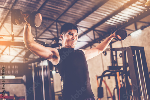 Portrait of a male muscular bodybuilder workout with dumbbell in fitness gym.