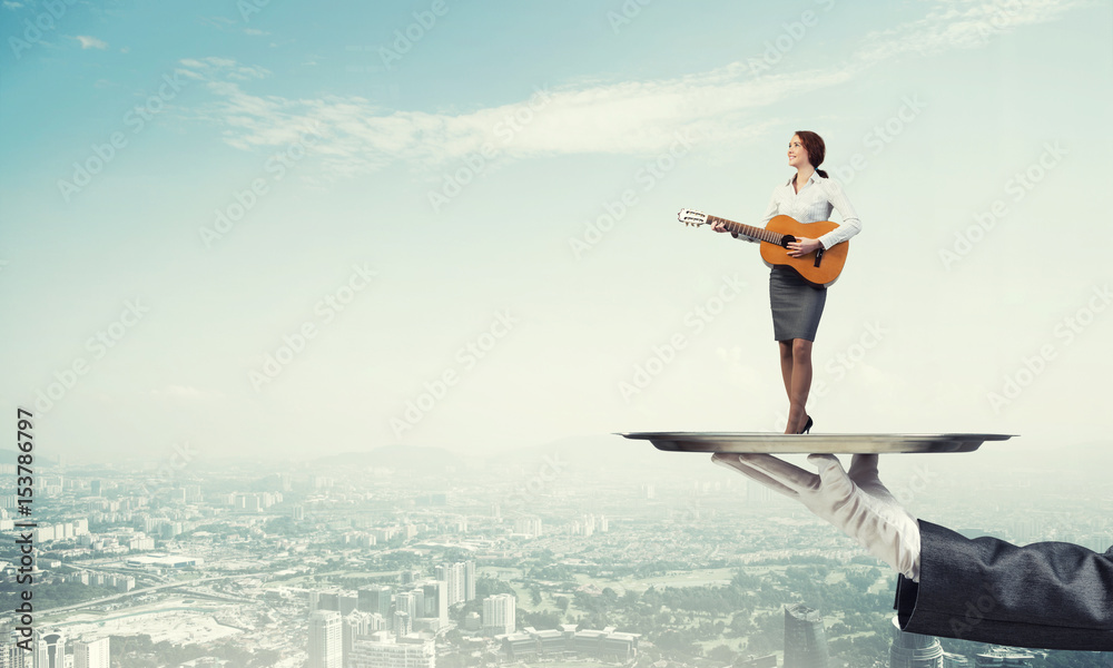 Attractive businesswoman on metal tray playing acoustic guitar against cityscape background Attractive businesswoman on metal tray playing acoustic guitar against cityscape background