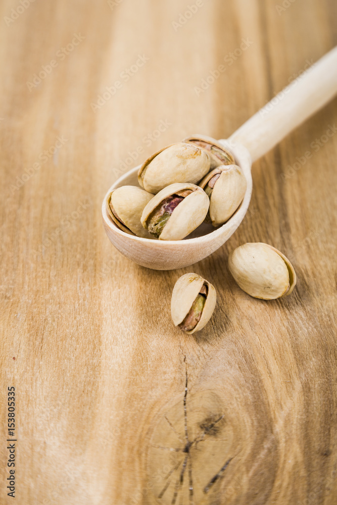 Pistachios in a spoon on a wooden table close up.