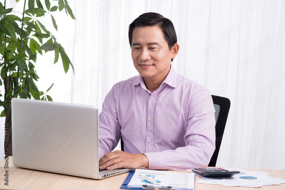 Fototapeta premium Business asian man sitting at his desk working on a computer and looking concentrated