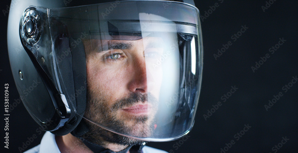 Fototapeta premium Portrait of a professional rider or motorcyclist, in a protective black helmet, on a black background. Concept: driver, drive, speed, protection, protective suit, reaction, love of extreme sports. 