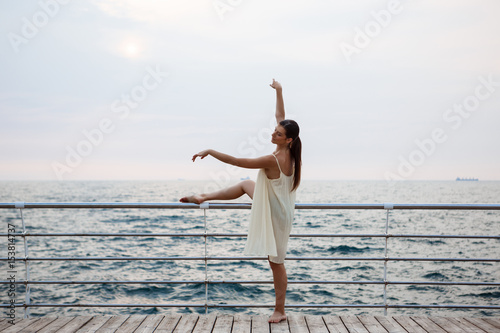 Young beautiful ballerina dancing and posing outside, sea background.
