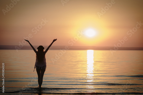 Silhouette of woman wearing hat with open arms under the sunrise near the sea