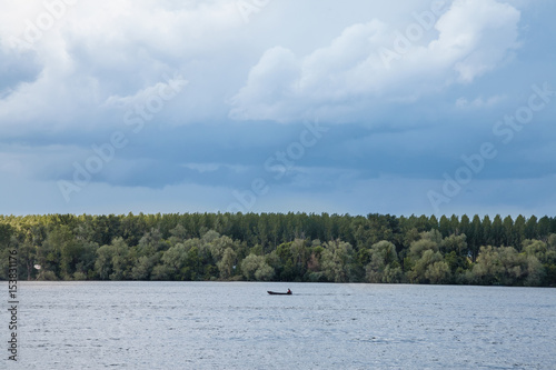 Picture of a boat on a canadian style lake, during a cloudy afternoon.