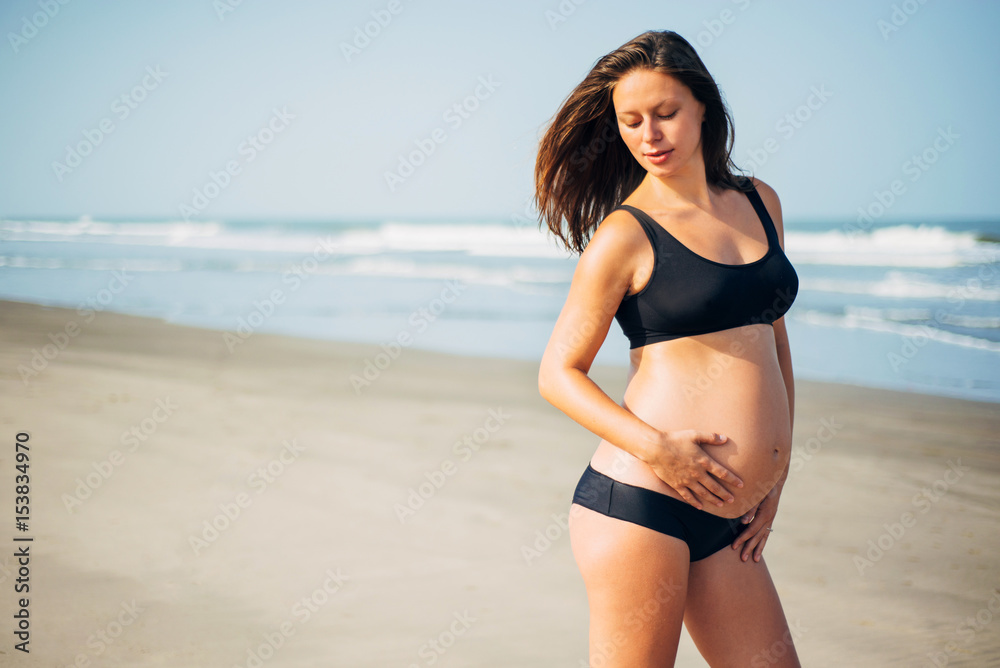 Portrait of beautiful happy dark-hear pregnant woman in black bikini on the beach Portrait of beautiful happy dark-hear pregnant woman in black bikini on the beach