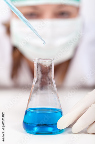 Laboratory technician dropping reagent into an erlenmeyer flask