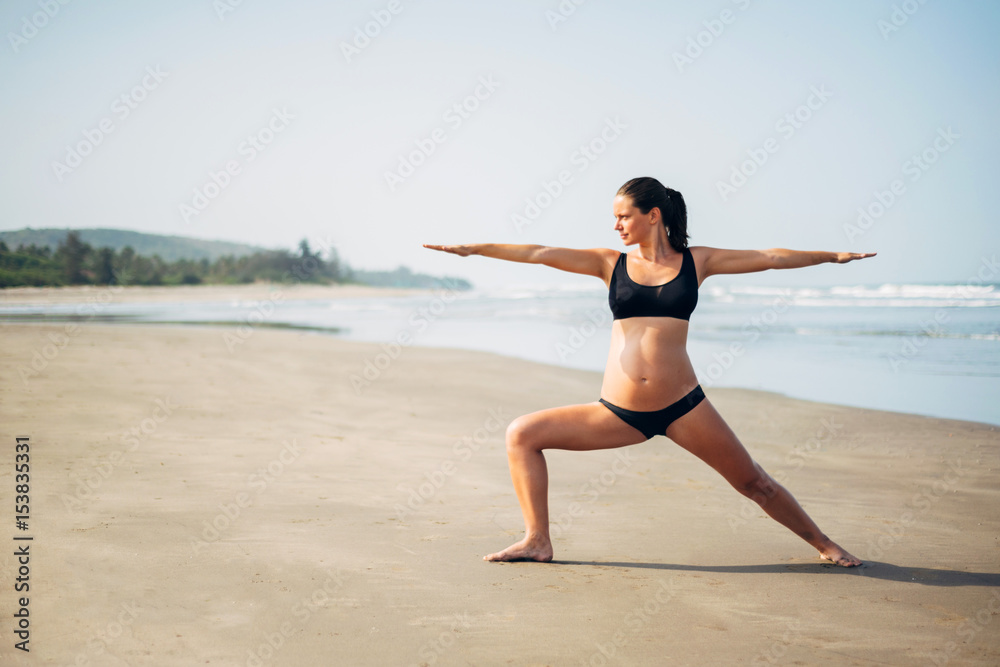 Pregnant woman on the beach doing yoga. Pregnant doing virabhadrasana. Pregnant woman doing workout near the the sea.