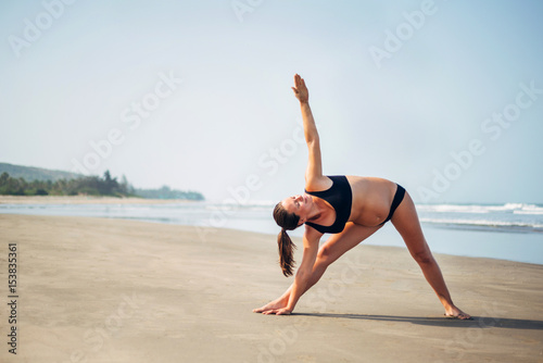Pregnant woman on the beach doing yoga. Pregnant doing utthita trikonasana. Pregnant woman doing workout near the the sea.