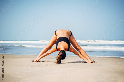 Pregnant woman on the beach doing yoga. Pregnant woman doing prasarita padhottanasana.Pregnant woman doing workout near the the sea. © innatyshchenko