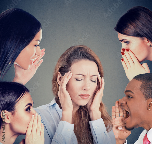 Group of people whispering gossip to a stressed woman suffering from headache photo