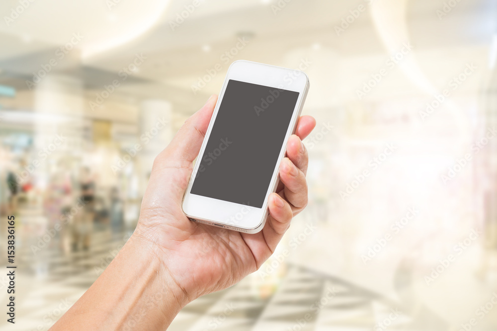 Hand holding mobile phone with abstract blur shopping mall background Hand holding mobile phone with abstract blur shopping mall background