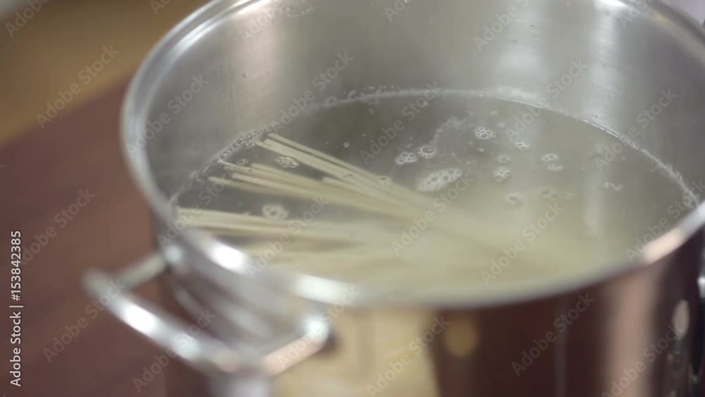 Detail of woman pouring spaghetti on saucepan, young woman preparing meal at the kitchen table. Detail of woman pouring spaghetti on saucepan, young woman preparing meal at the kitchen table.