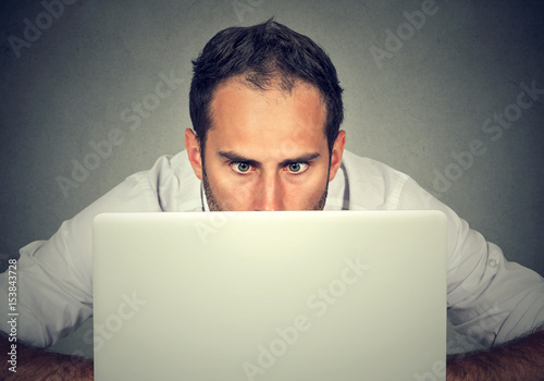 Man hiding behind a laptop staring at screen with a shocked face expression