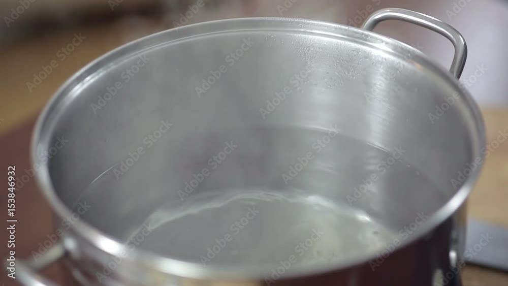 Detail of boiling water on saucepan, young woman preparing meal at the kitchen table. Detail of boiling water on saucepan, young woman preparing meal at the kitchen table.