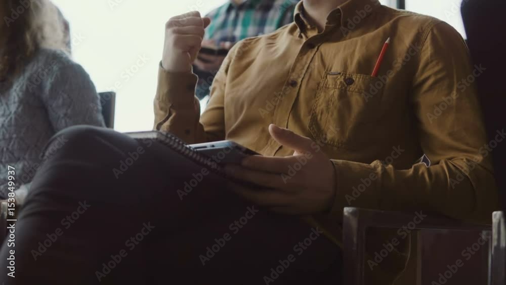 Close-up view of young businessman sitting at seminar and making notes at tablet. Man at loft office with young team. Close-up view of young businessman sitting at seminar and making notes at tablet. Man at loft office with young team.