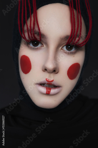 Creative beauty with geometric make up on a woman. red stripe on lips, red circles on cheeks, red threads on eyelashes. dark background