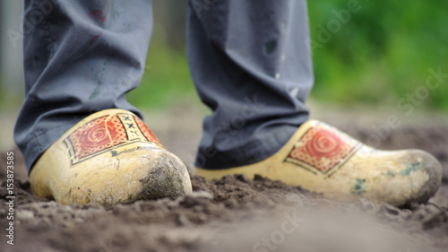 Canvas Print Dutch clogs on the feet of a worker, worn out and standing in loose sand, some g