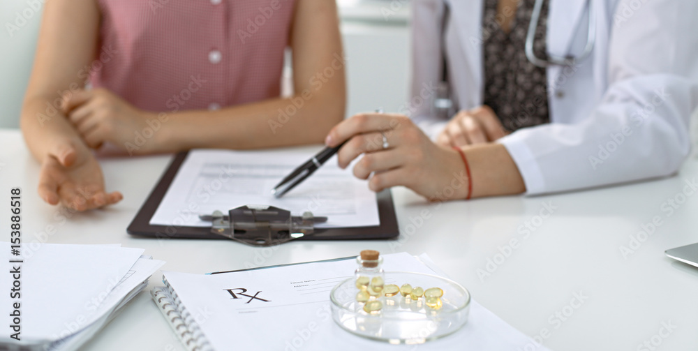 Medical prescription form, capsules and pills are lying against the background of a doctor and patient discussing health exam results 