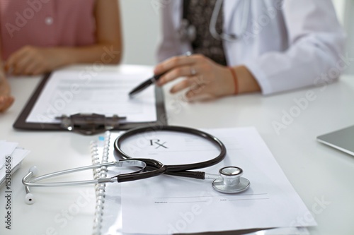 Stethoscope, medical prescription form are lying against the background of a doctor and patient discussing health exam results 